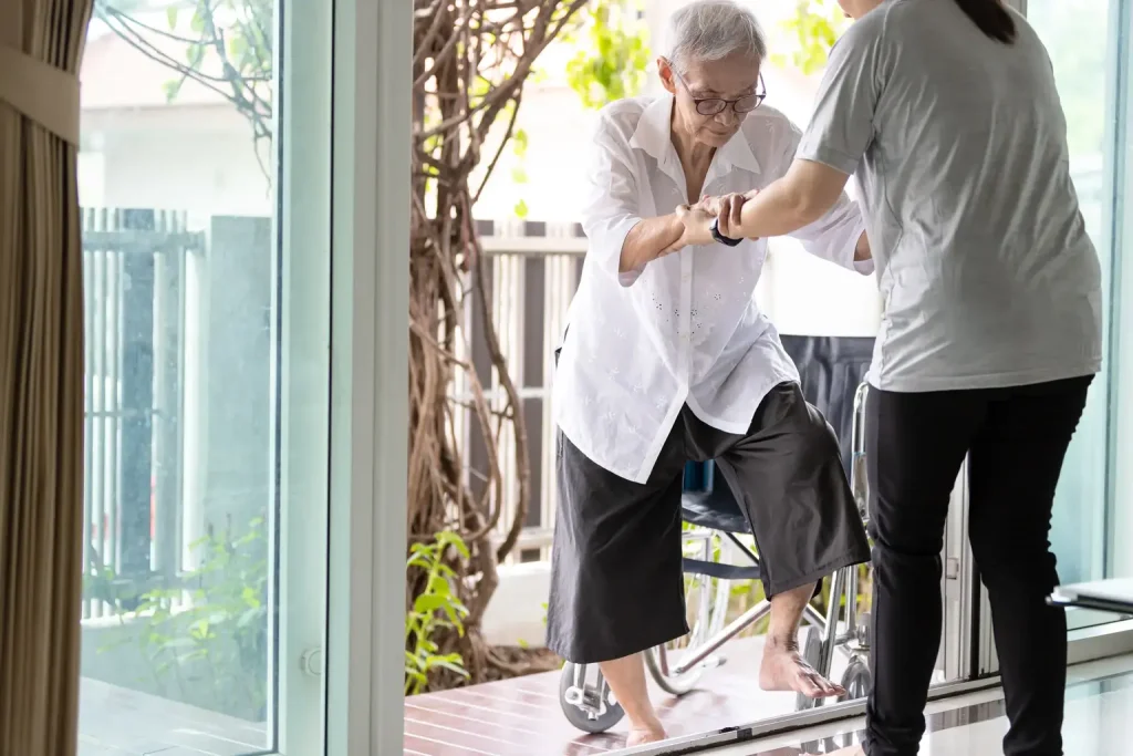 Nurse helping elderly woman out of her wheelchair and assisting her to walk inside