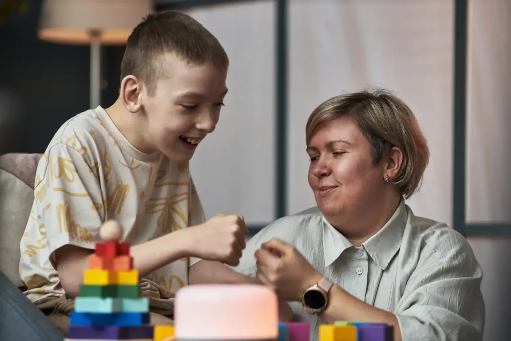 young disabled boy and female support worker fist bumping and playing with toys